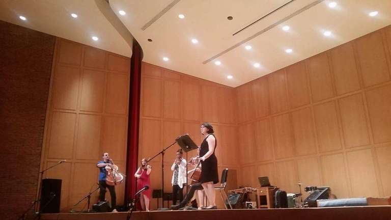 A long shot of Jamie singing into a microphone on stage with instrumentalists.
