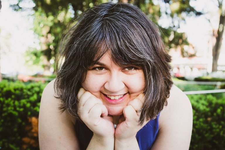 Jamie holds her face in her hands and smiles at the camera.